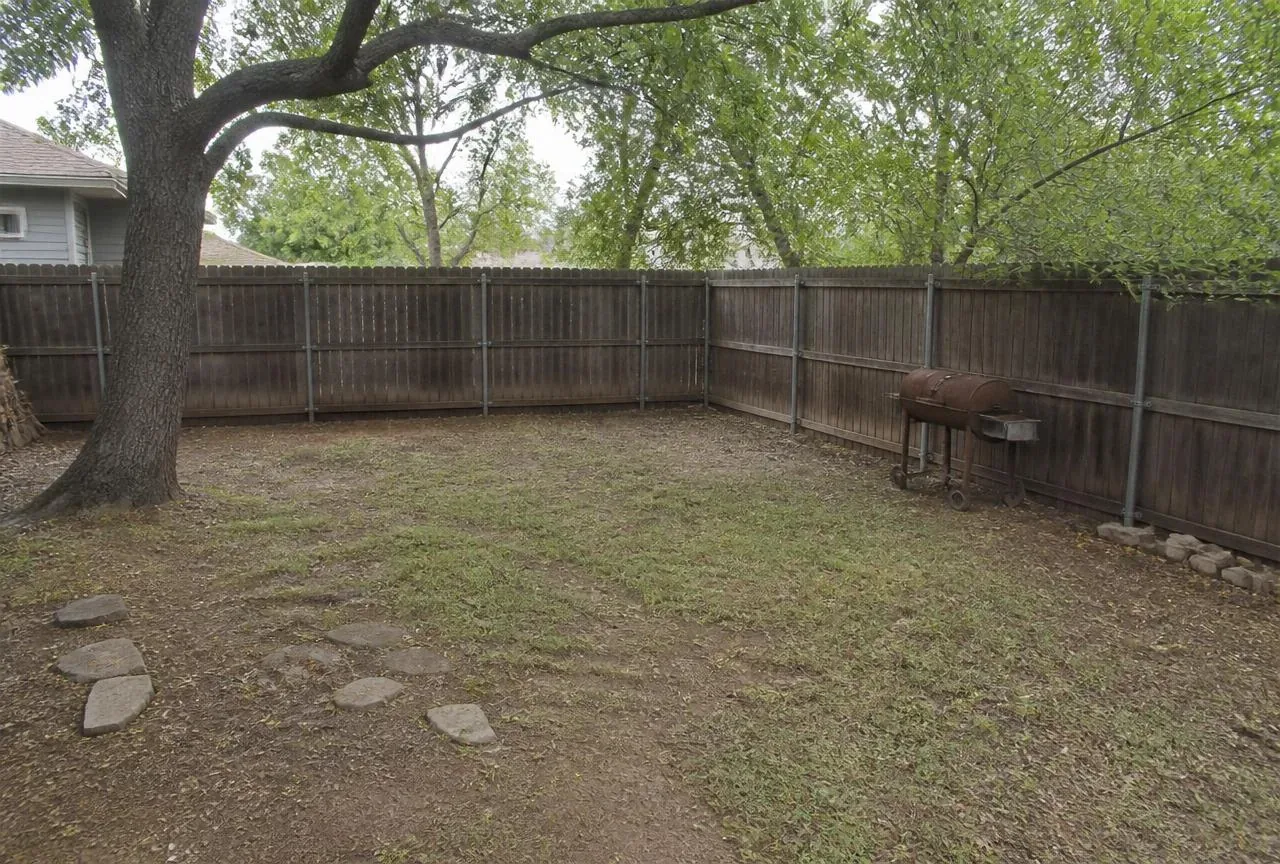 Before: Bare worn backyard corner under a large tree with an old grill before construction