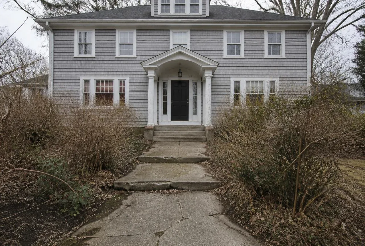 Before: Cracked concrete front walk and overgrown shrubs at a grey shingled colonial before work