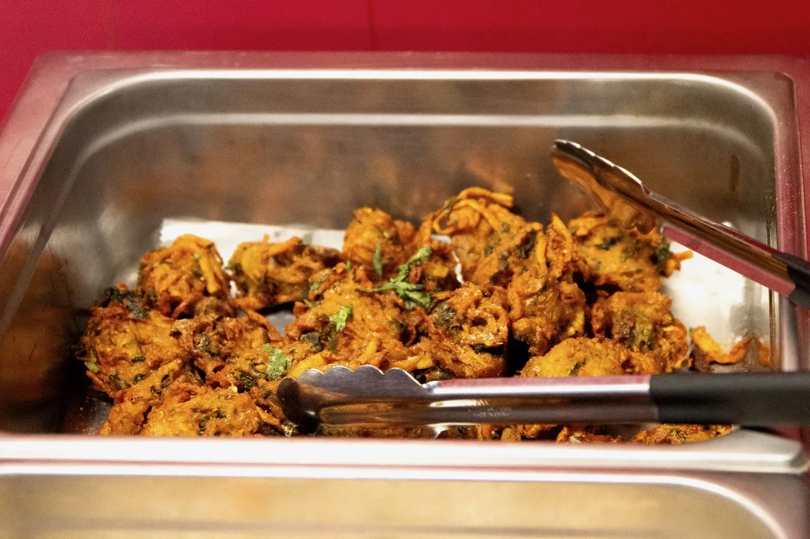 Crispy fried pakoras with serving tongs