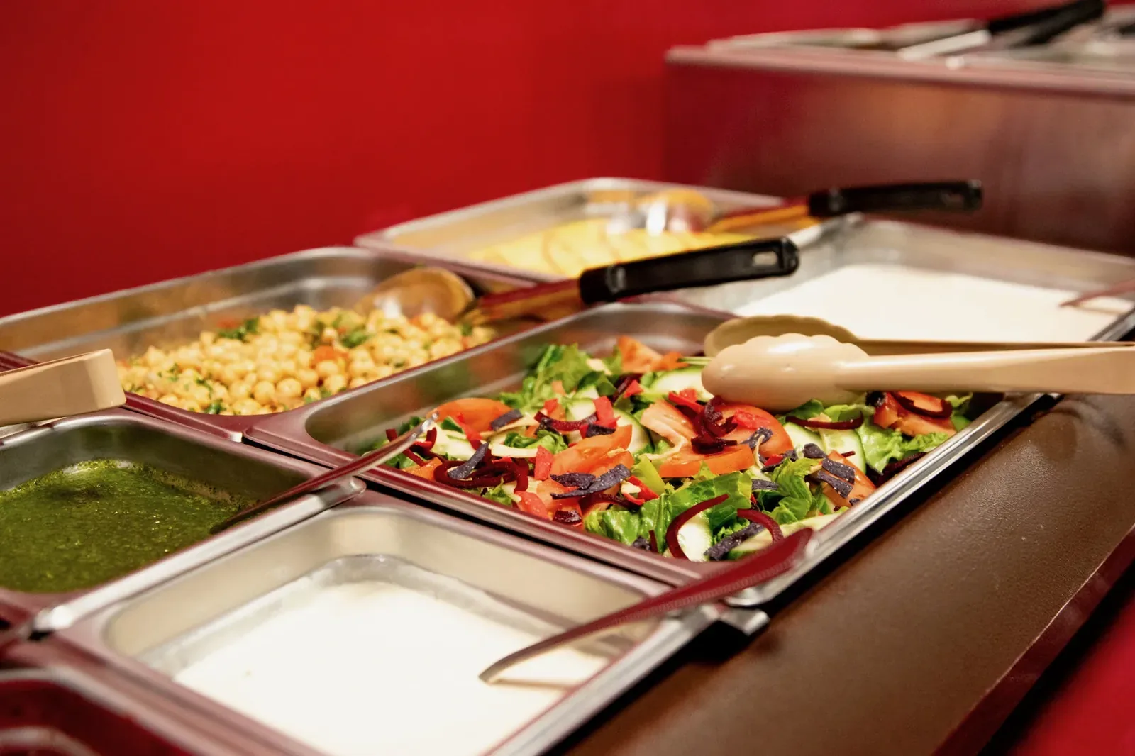 Salad bar with chickpea salad, sliced vegetables, mint chutney and raita