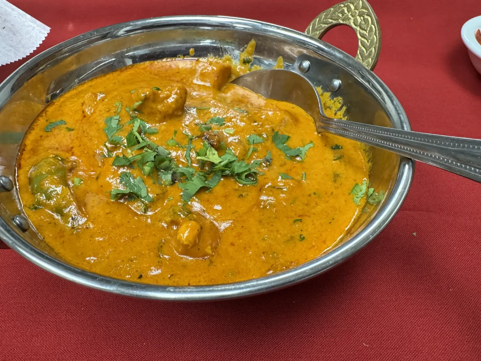 Chicken curry served in a brass-handled kadai on a red tablecloth