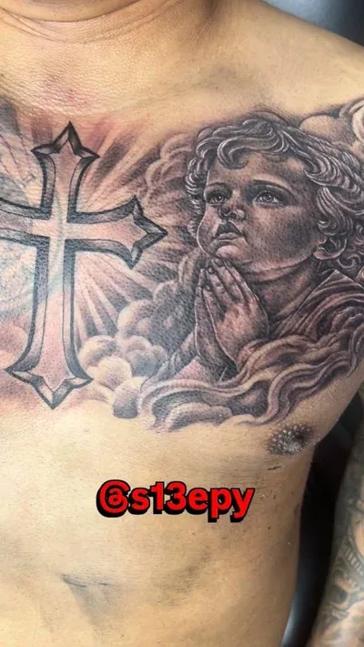Black and grey chest tattoo of a cross and a praying angel